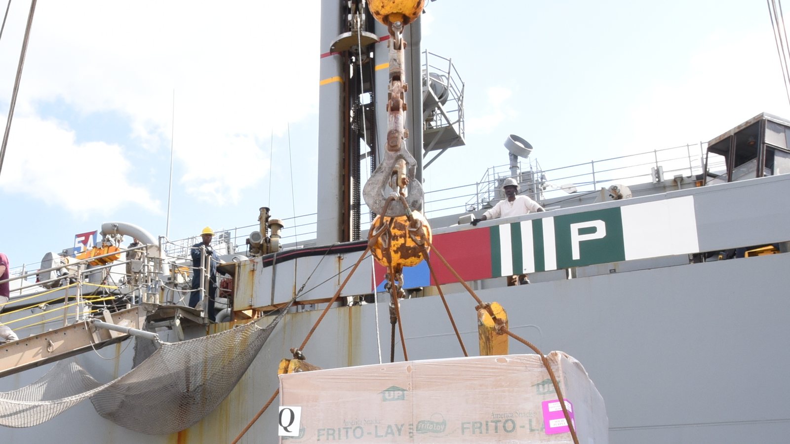 A ship&rsquo;s crane lifting a slung pallet of stores aboard from the supply boat alongside